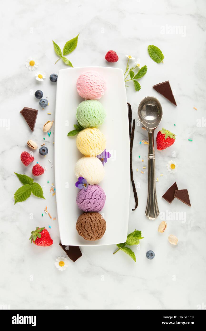 Set aus verschiedenen Eislöffeln und Beeren auf weißem Marmorhintergrund. Erdbeere, Pistazien, Mango, Vanille, Heidelbeere und Schokoladeneis. Oben Stockfoto