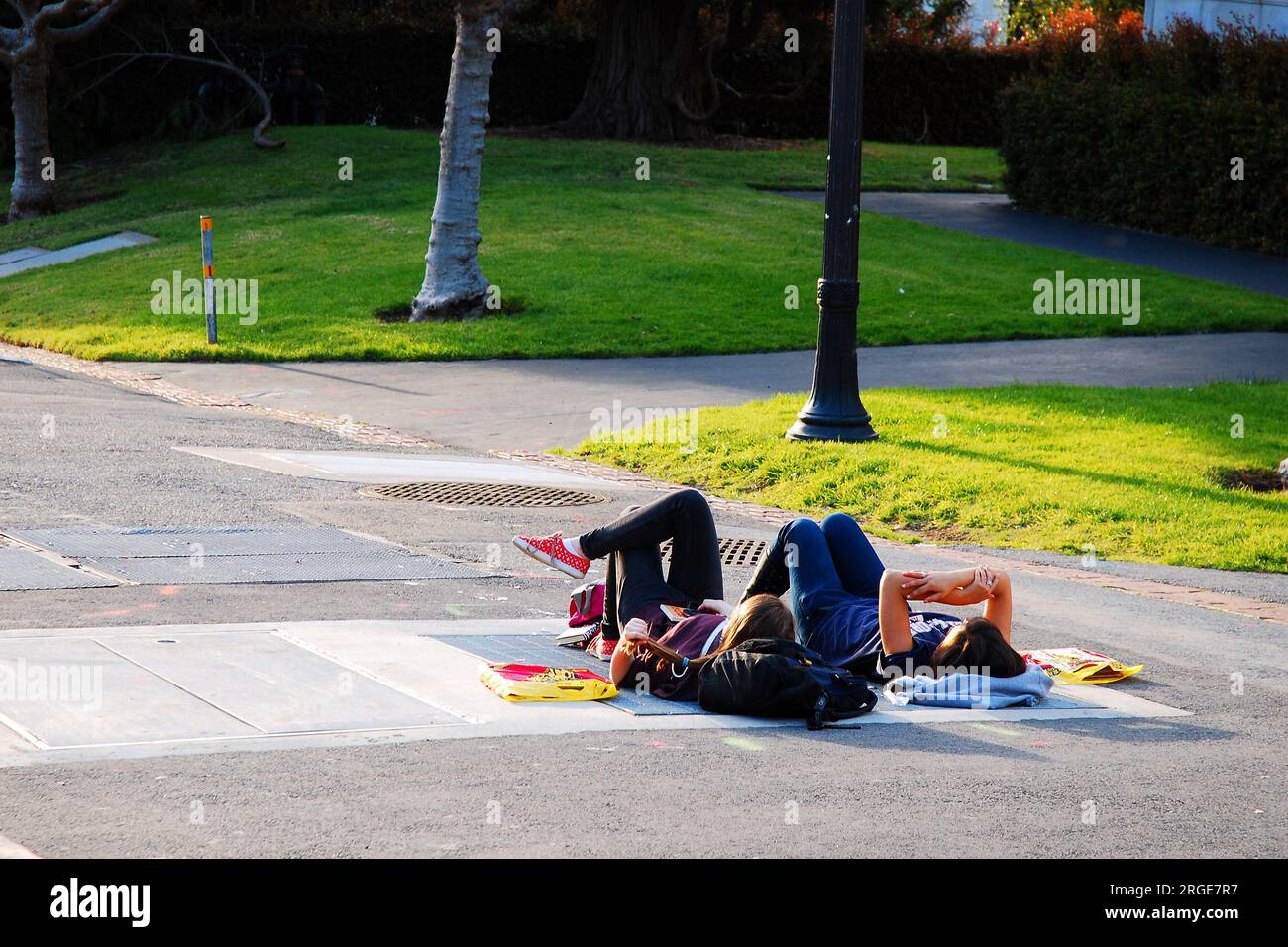 Zwei Studenten liegen auf dem Fußweg auf dem Campus der University of California Berkeley, um den Sonnenuntergang zu beobachten Stockfoto
