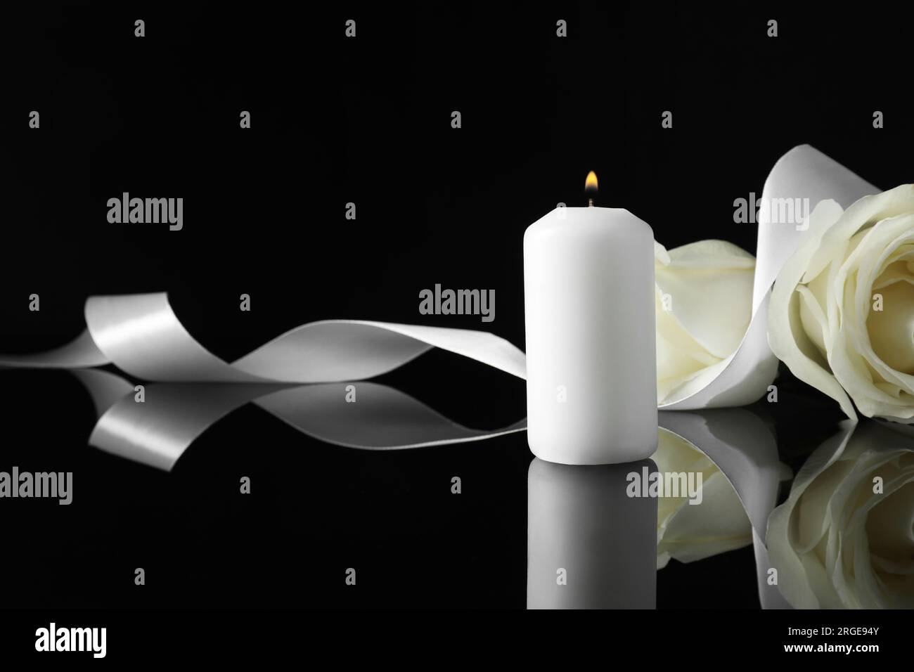 Brennende Kerze, weiße Rosen und Band auf schwarzer Spiegeloberfläche bei Dunkelheit, Platz für Text. Begräbnissymbole Stockfoto