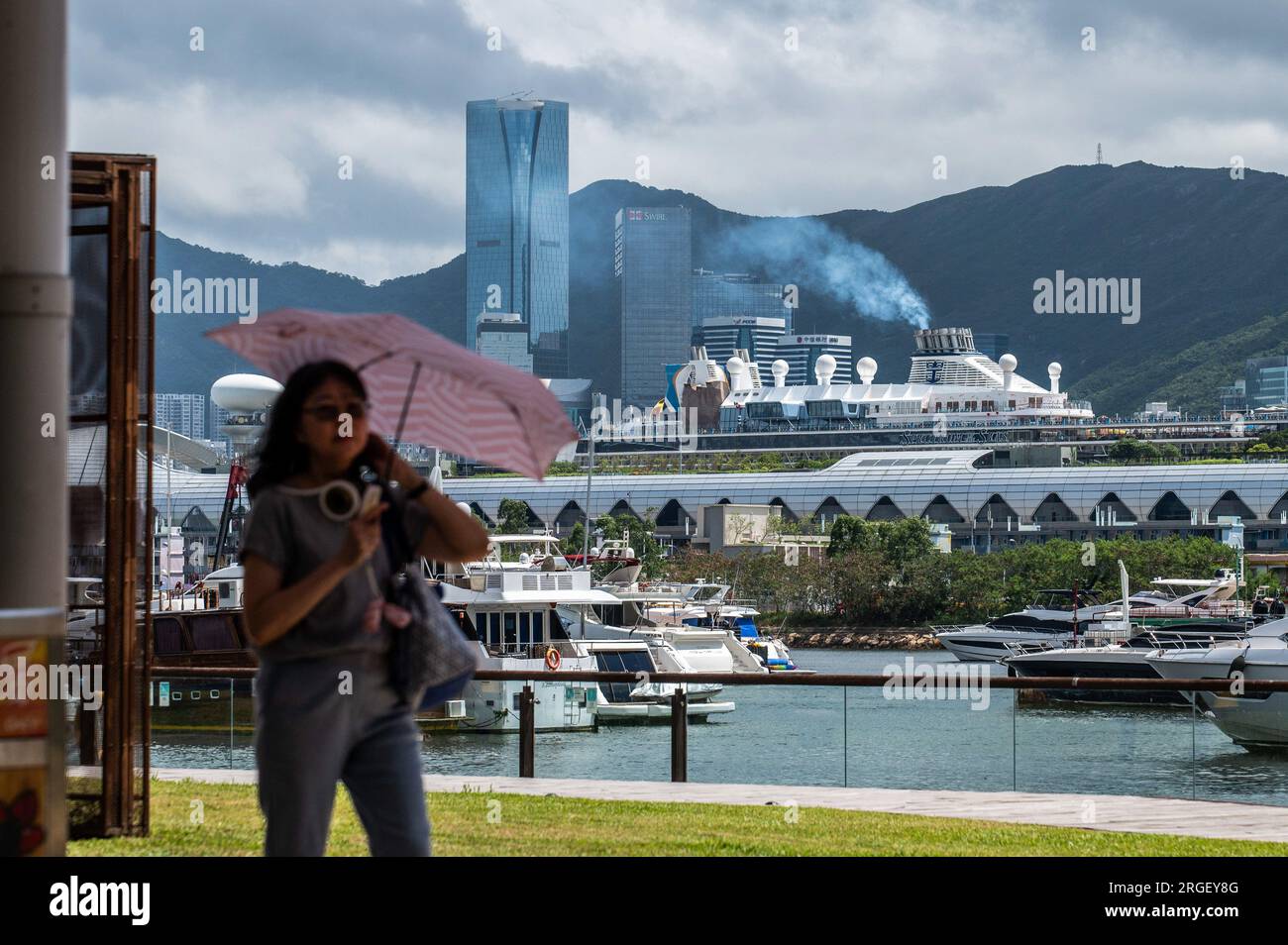 Hongkong. 05. Aug. 2023. Eine Frau geht entlang der Kwun Tong Promenade, während ein Kreuzfahrtschiff am nahe gelegenen Kai Tak Cruise Terminal anlegt. Da 18 Kreuzfahrtlinien planen, Hongkong zu besuchen, die Hunderte von Schiffen anlaufen, wird sich das Problem der Emissionen am Hafen für die Einwohner nur noch verschärfen, von denen viele keine andere Wahl haben, als in der Nähe dieser Schadstoffemittenten zu leben. (Foto: Ben Marans/SOPA Images/Sipa USA) Guthaben: SIPA USA/Alamy Live News Stockfoto