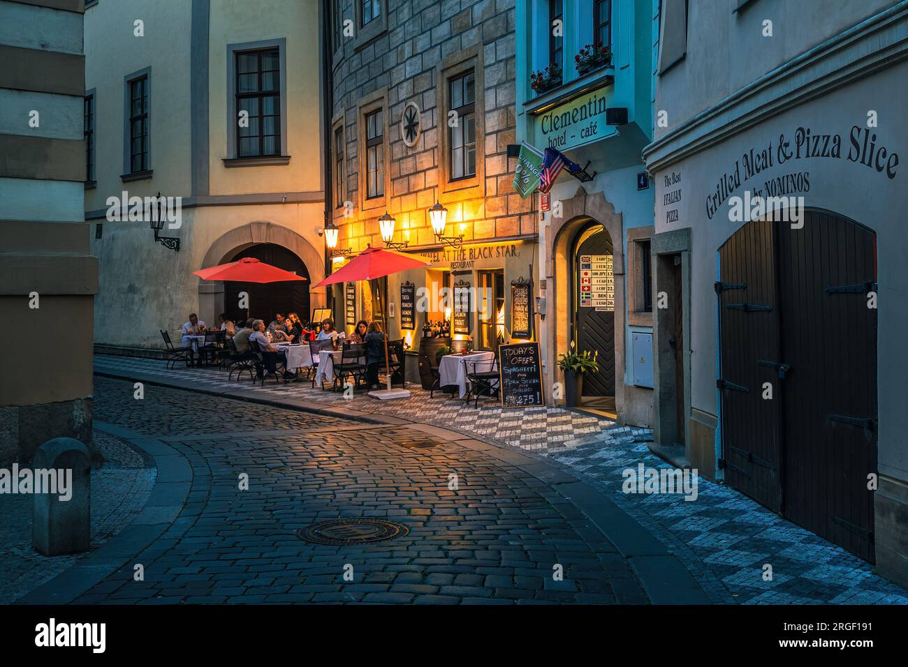 Kleines Restaurant im Freien auf der engen Kopfsteinpflasterstraße, beleuchtet von Lichtern in der Altstadt von Prag, Tschechische Republik. Stockfoto