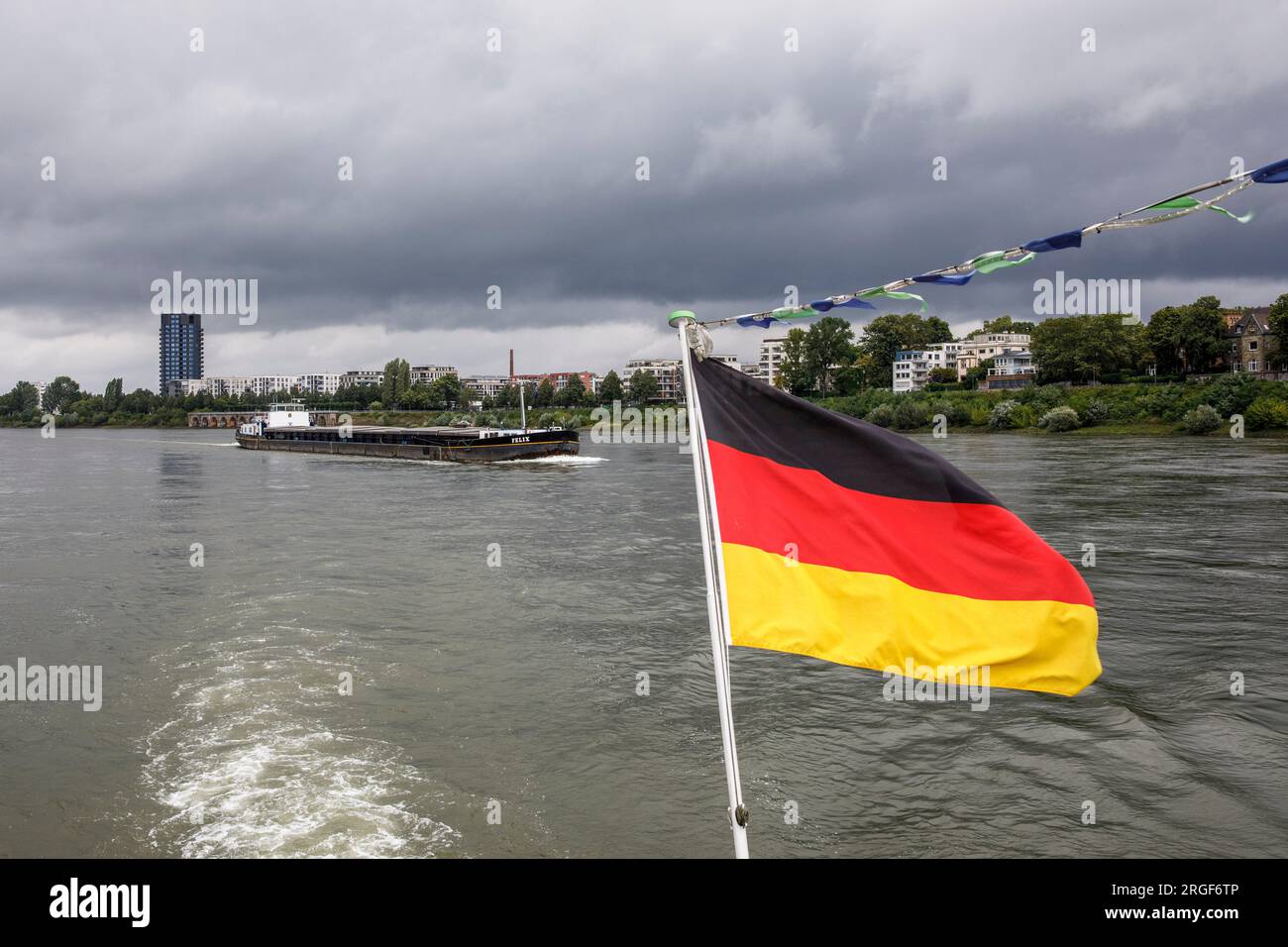 Frachtschiff auf dem Rhein, Rheinufer im Bezirk Mülheim, deutsche Flagge auf einem Ausflugsboot, Köln, Deutschland. Frachtschiff auf dem Rhein, R Stockfoto