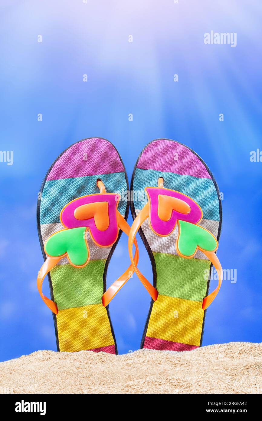 Mehrfarbige Flip-Flops, Schiefer mit Herz auf Sand. Sonniger Tag. Urlaub, Meer, Valentinstag am Strand. Vertikal. Speicherplatz kopieren Stockfoto