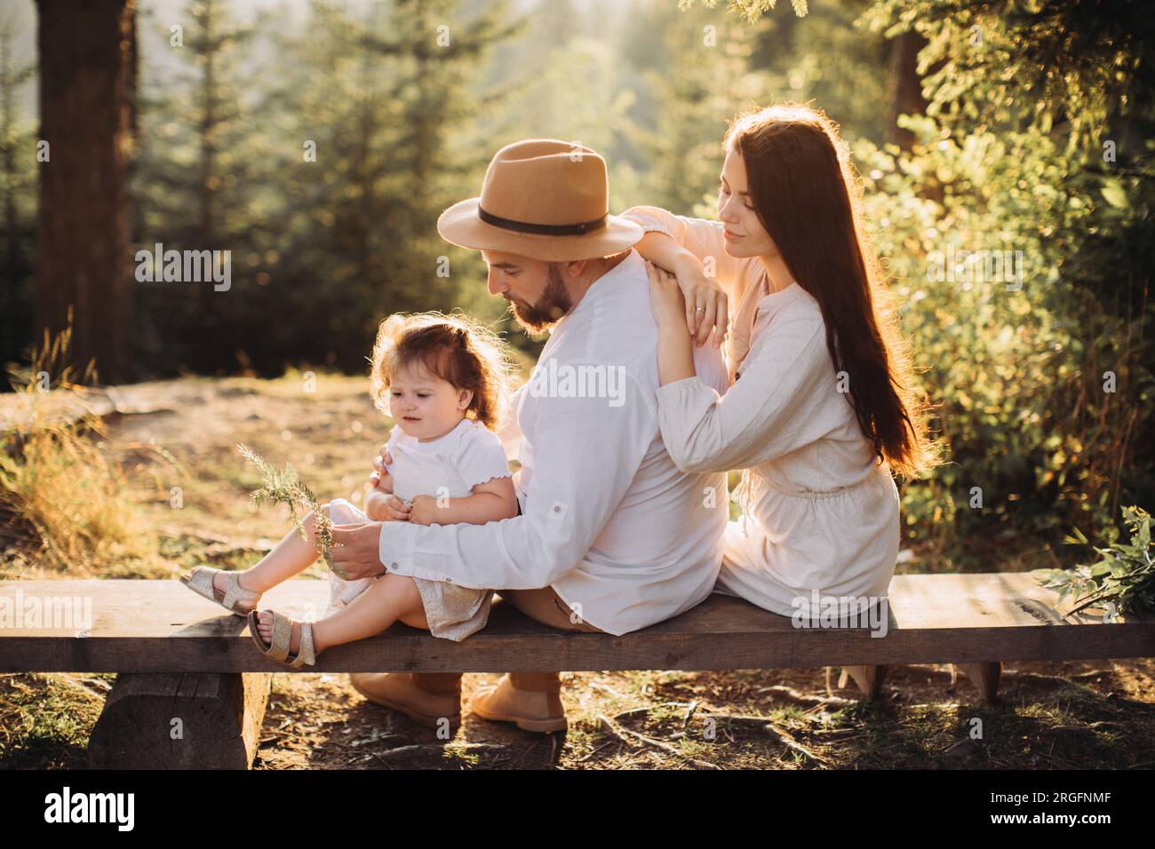 Junge Familie sitzt auf einer Bank im sonnigen Wald Stockfoto