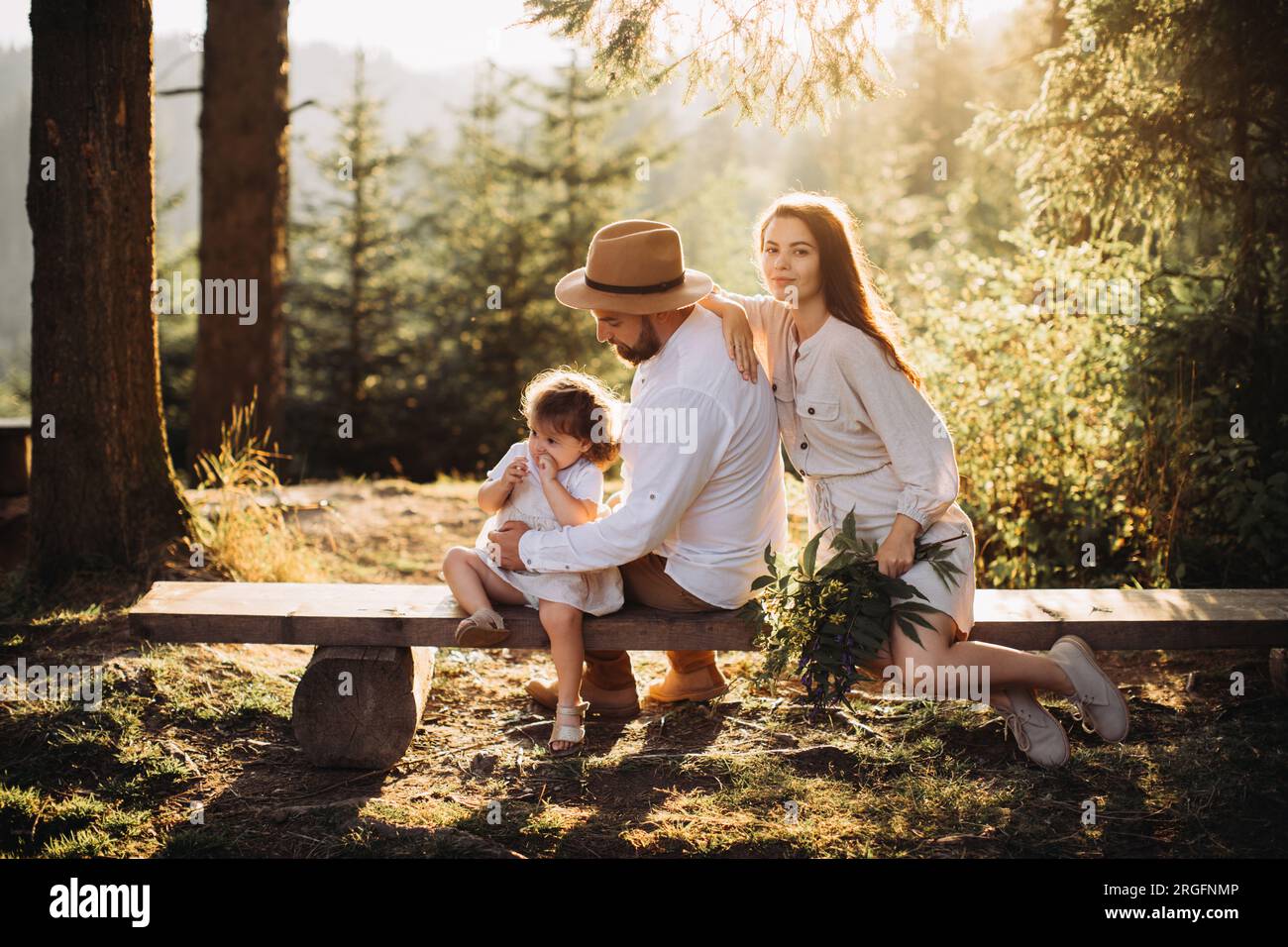 Junge Familie sitzt auf einer Bank im sonnigen Wald Stockfoto