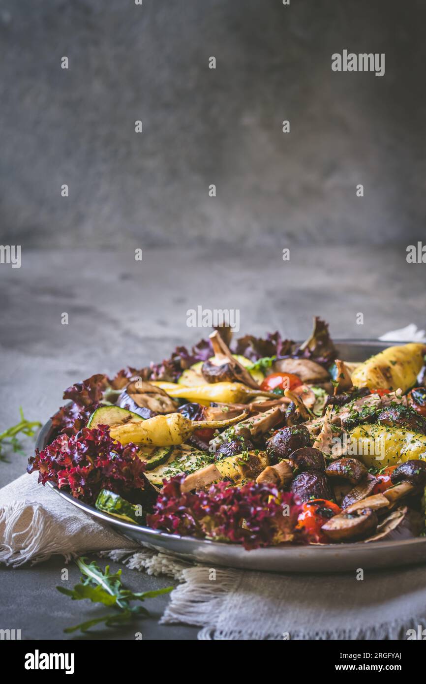 Gegrilltes Gemüse mit Salat und Oliven, italienisches Antipasti, grauer Hintergrund, vertikal mit Kopierbereich Stockfoto