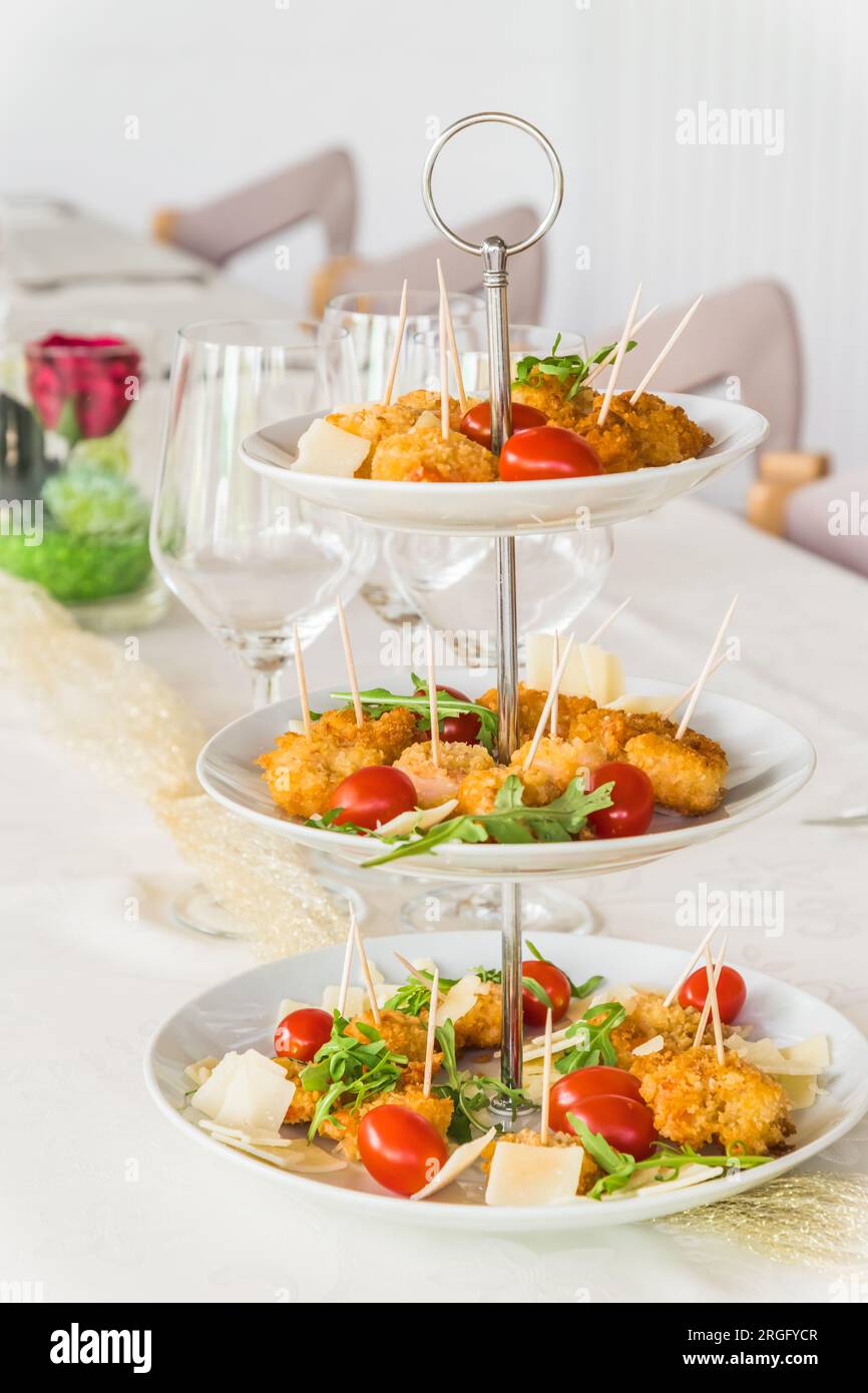 Gebratene panierte Garnelen mit Rucolasalat auf einem Porzellankuchenstand auf einem weißen, eleganten, vertikalen Tisch Stockfoto