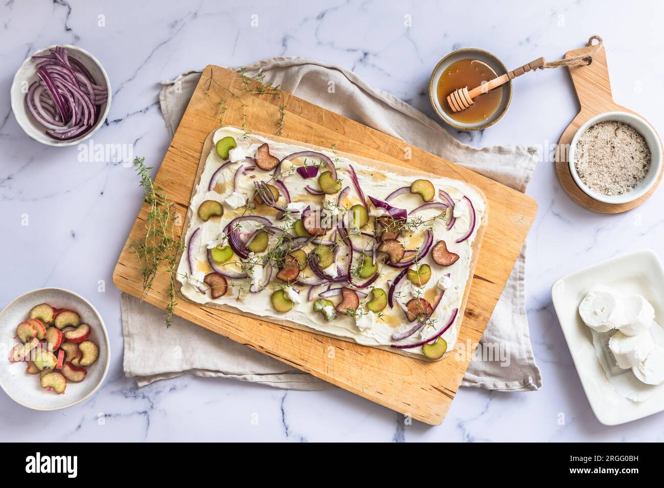 flammkuchen mit Rhabarber, roten Zwiebeln, Ziegenkäse und Honig, zum Backen zubereitet, Marmorhintergrund, Blick von oben Stockfoto