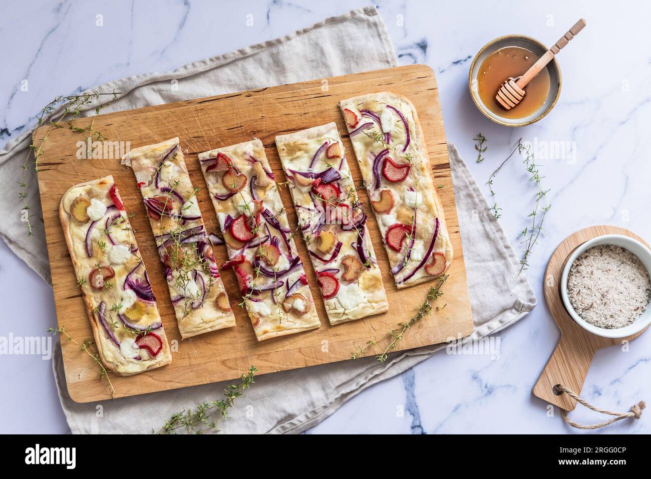 Gebackene Tarte Flambee mit Rhabarber, roten Zwiebeln, Ziegenkäse und Honig, in Streifen geschnitten, Marmorhintergrund, Draufsicht Stockfoto