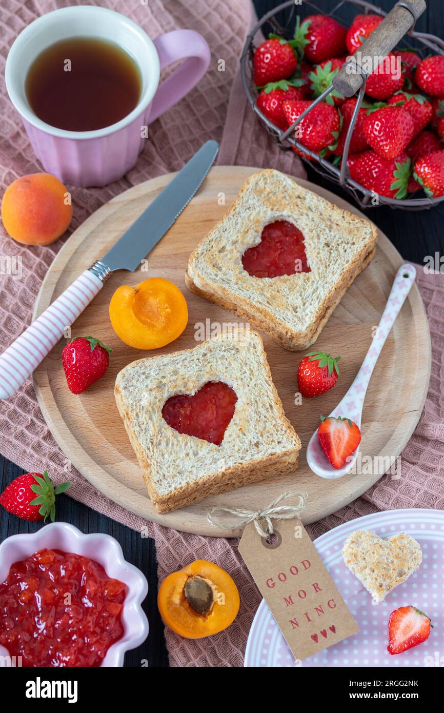 Frühstückstisch mit Erdbeermarmelade Toast, Tasse Tee und frischen Erdbeeren und Aprikosen Stockfoto