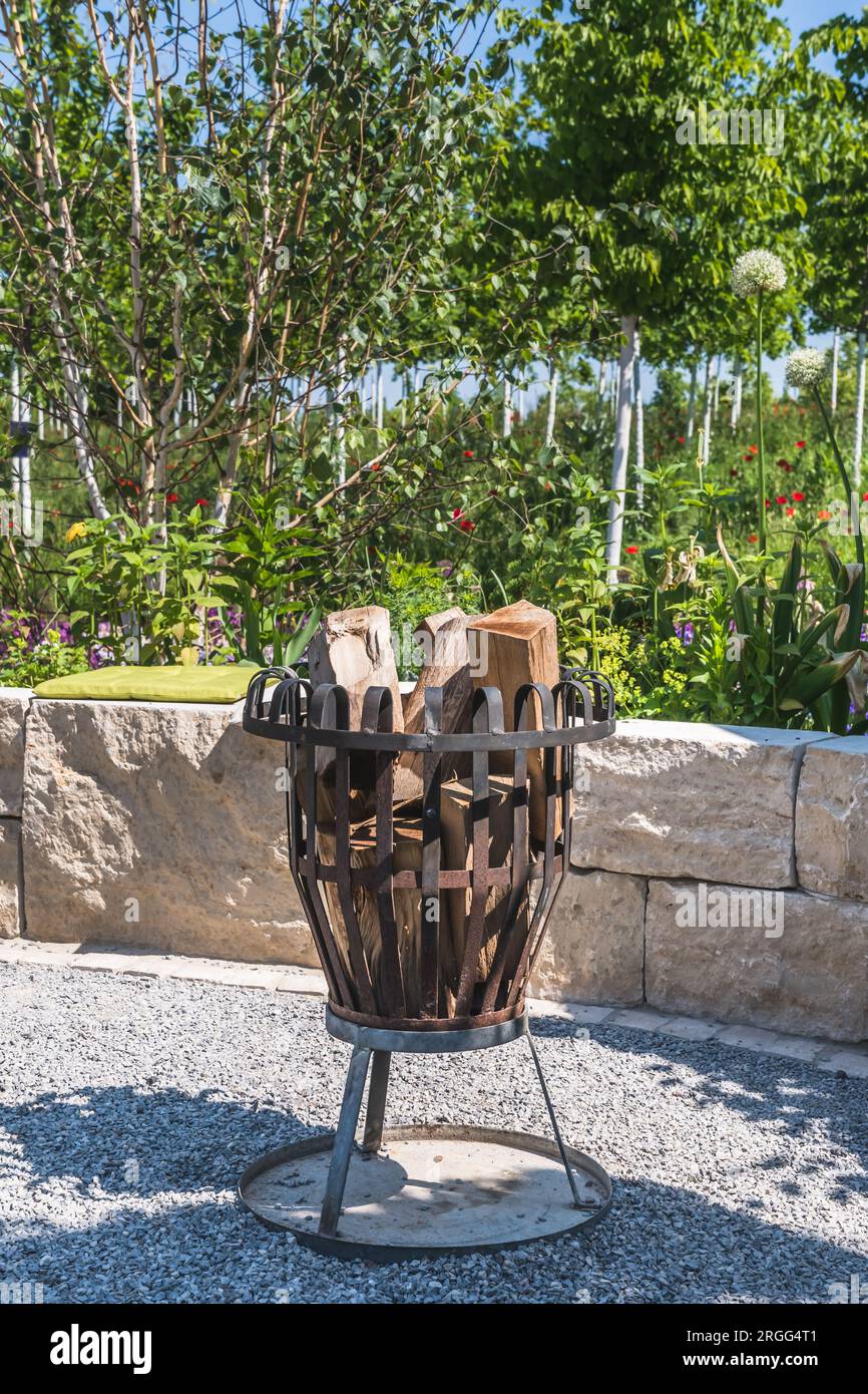 Metallfeuerkorb gefüllt mit Holz in einem Garten, vertikal Stockfoto