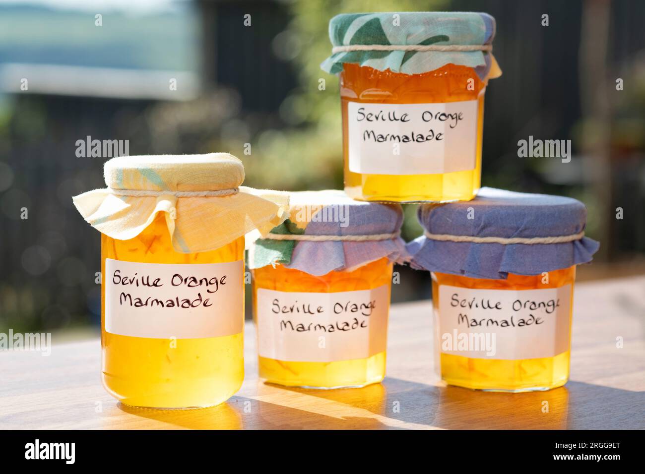 Eine Gruppe Gläser mit hausgemachter Sevilla-Orangenmarmelade. Die Gläser sind mit handgeschriebenen Etiketten und Stoffbeschichtungen über den Deckeln versehen Stockfoto