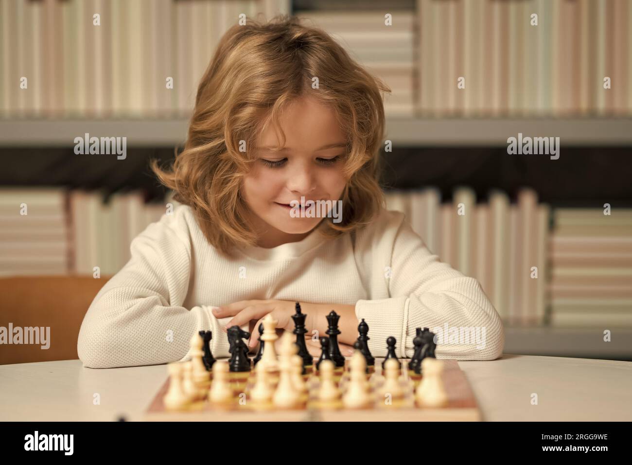 Kluges, konzentriertes und denkendes Kind, das Schach spielt. Kinder Frühentwicklung. Ein Junge, der zu Hause Schach spielt. Porträt aus der Nähe, komisches Gesicht. Stockfoto