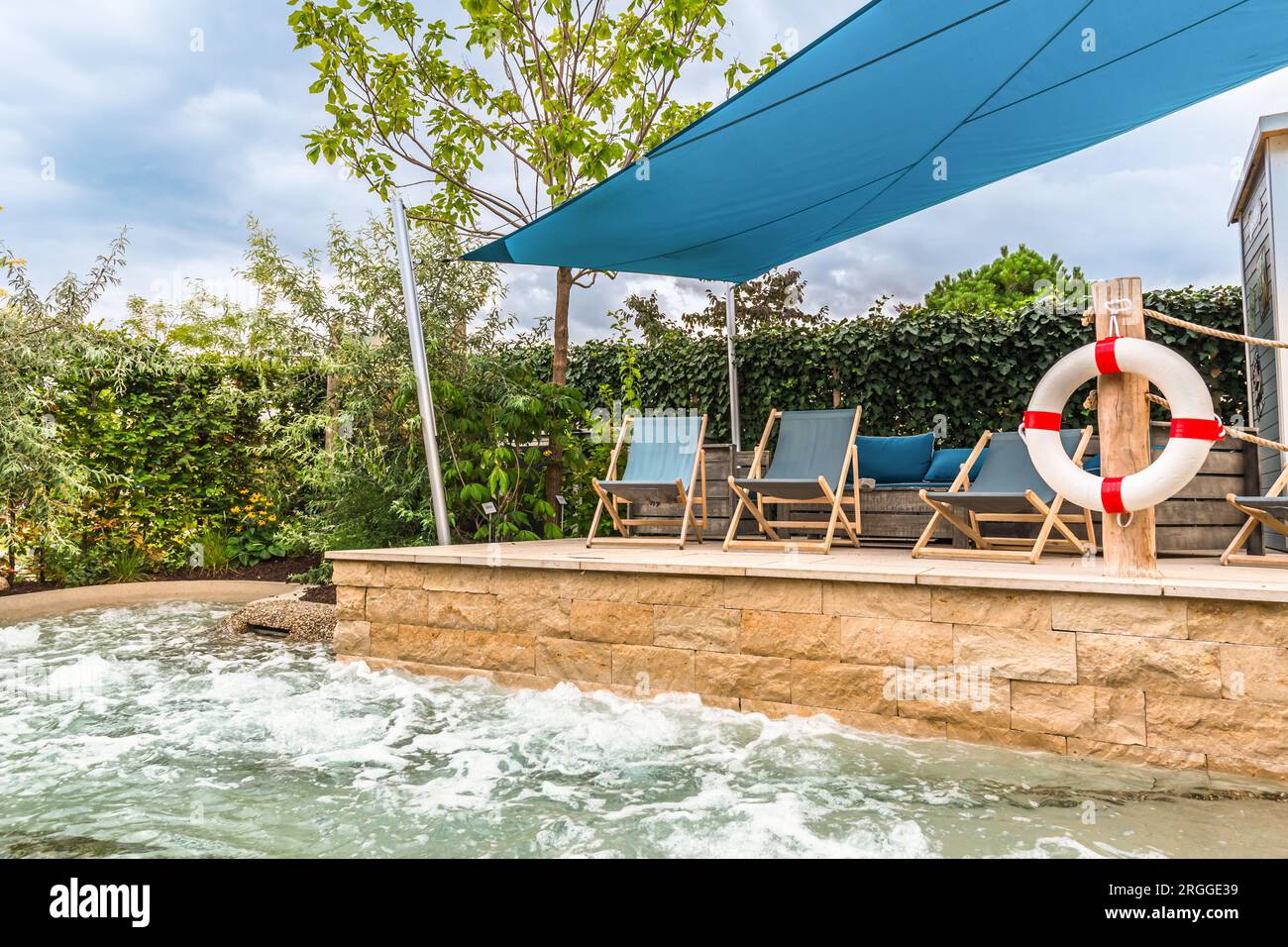 Terrasse mit Sonnenliegen am modernen eingebauten Whirlpool. Sprudelnder Swimmingpool, Wellnessbereich Stockfoto