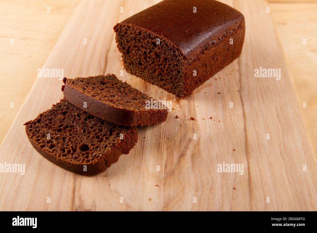 Dunkles Brotlaaf und seine geschnittenen Pendants auf hellem beigefarbenem Holzhintergrund Stockfoto