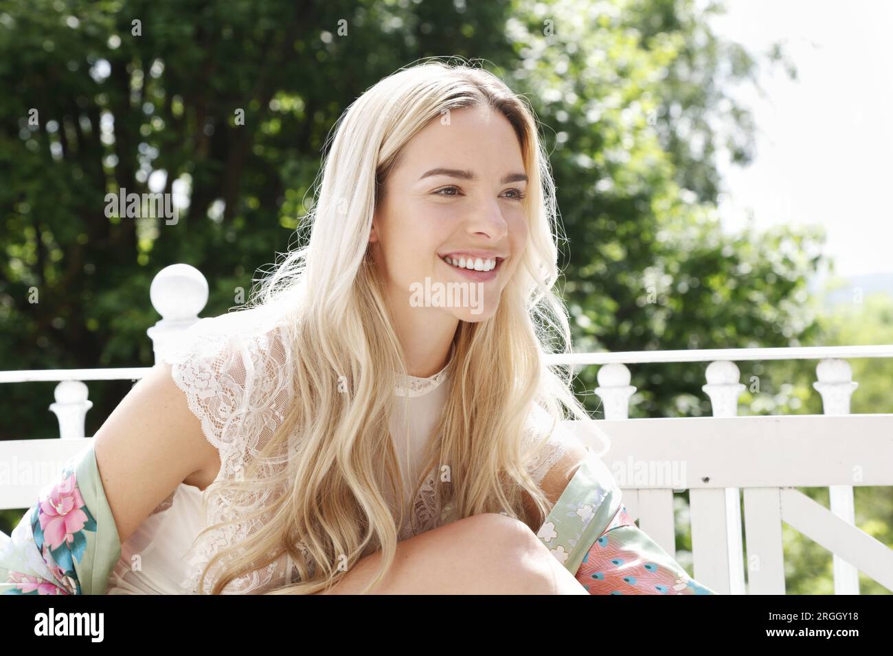 Lächelnde Frau, die an einem sonnigen Tag draußen sitzt Stockfoto