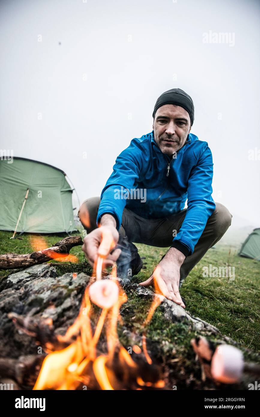 Man rösten mashmallows an nebligen Camp Stockfoto