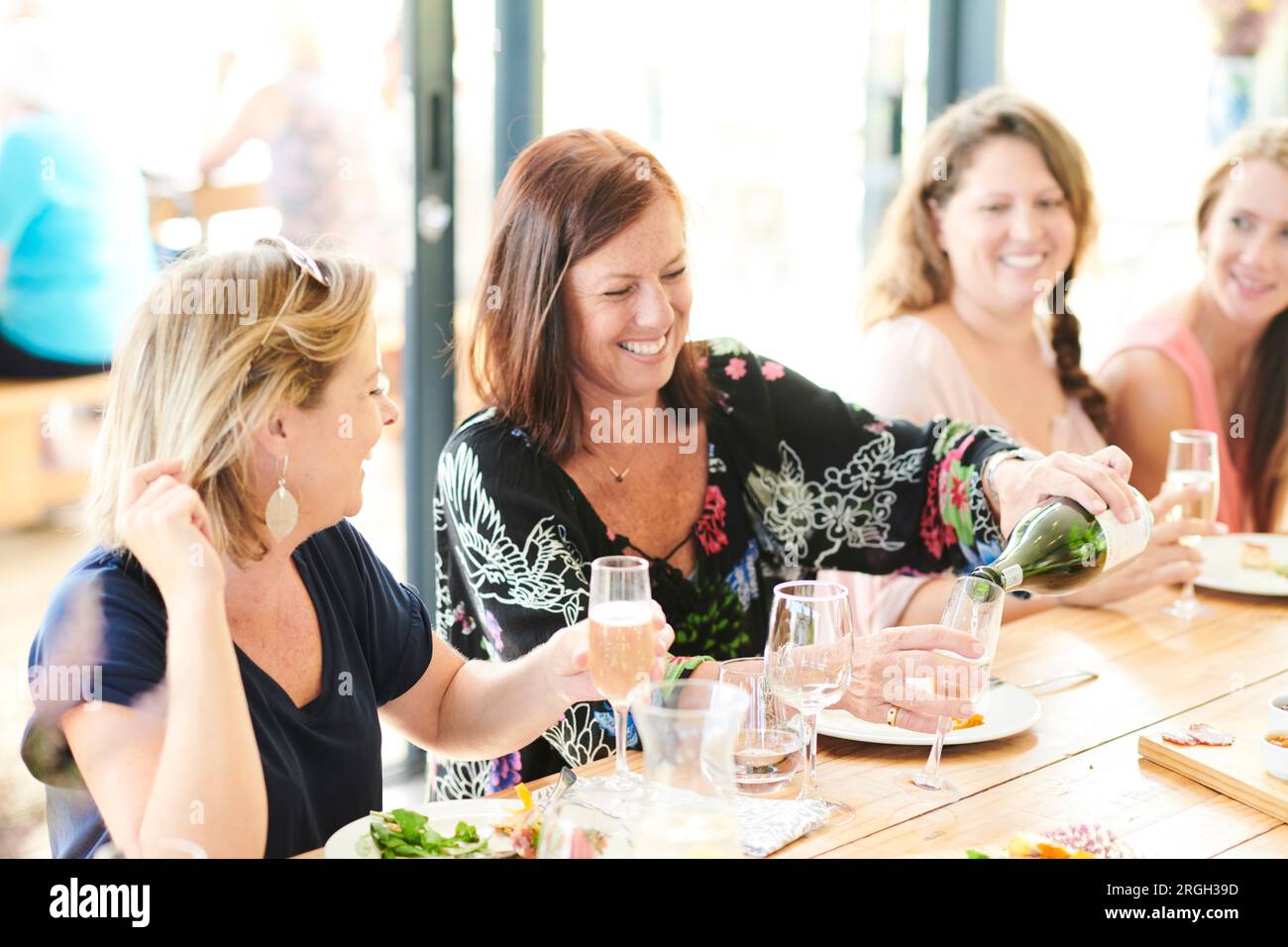 Lächelnde Frau giesst Wein mit Freunden Stockfoto