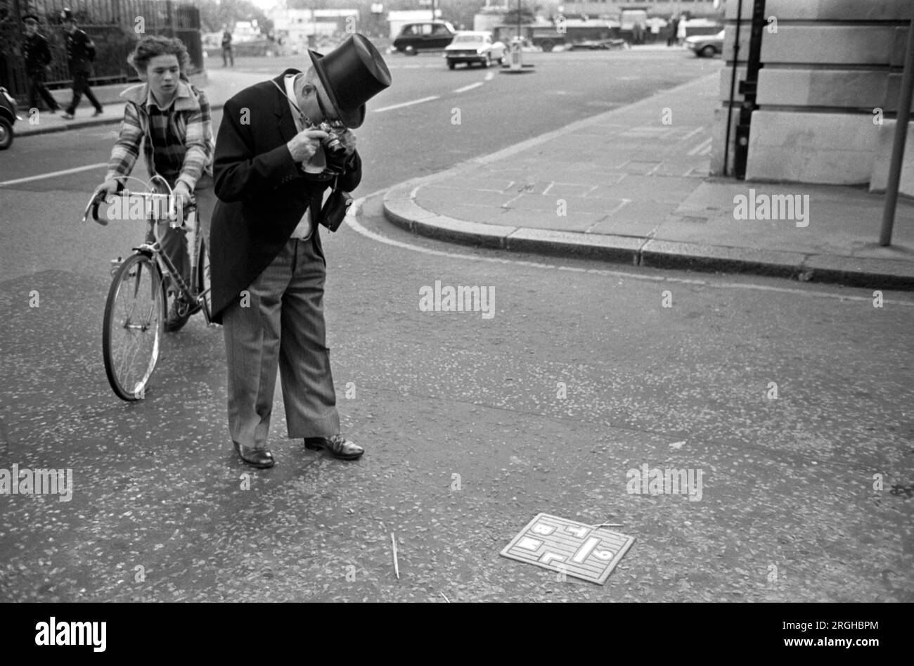 Es wird eine altmodische Filmkamera verwendet. Ein Mann mit Hut und Mantel, der seine Kamera überprüft. Indem Sie es auf den Boden richten, um die Funktionen zu prüfen. Er ist verkleidet und ein Hochzeitsgast. London 1975 England UK HOMER SYKES Stockfoto