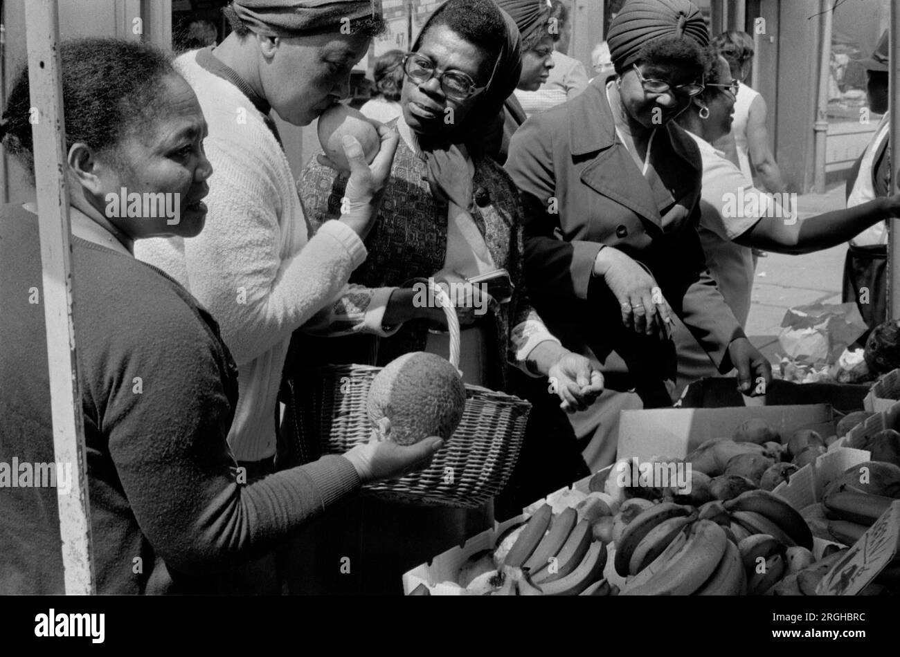 Multiethnisches Großbritannien 1970er Vereinigtes Königreich. Portobello Road Notting Hill London Samstag Marktstand. Eine Gruppe schwarzer britischer Frauen, die Obst kaufen, um zu sehen, ob sie reif sind. 1975, HOMER SYKES Stockfoto