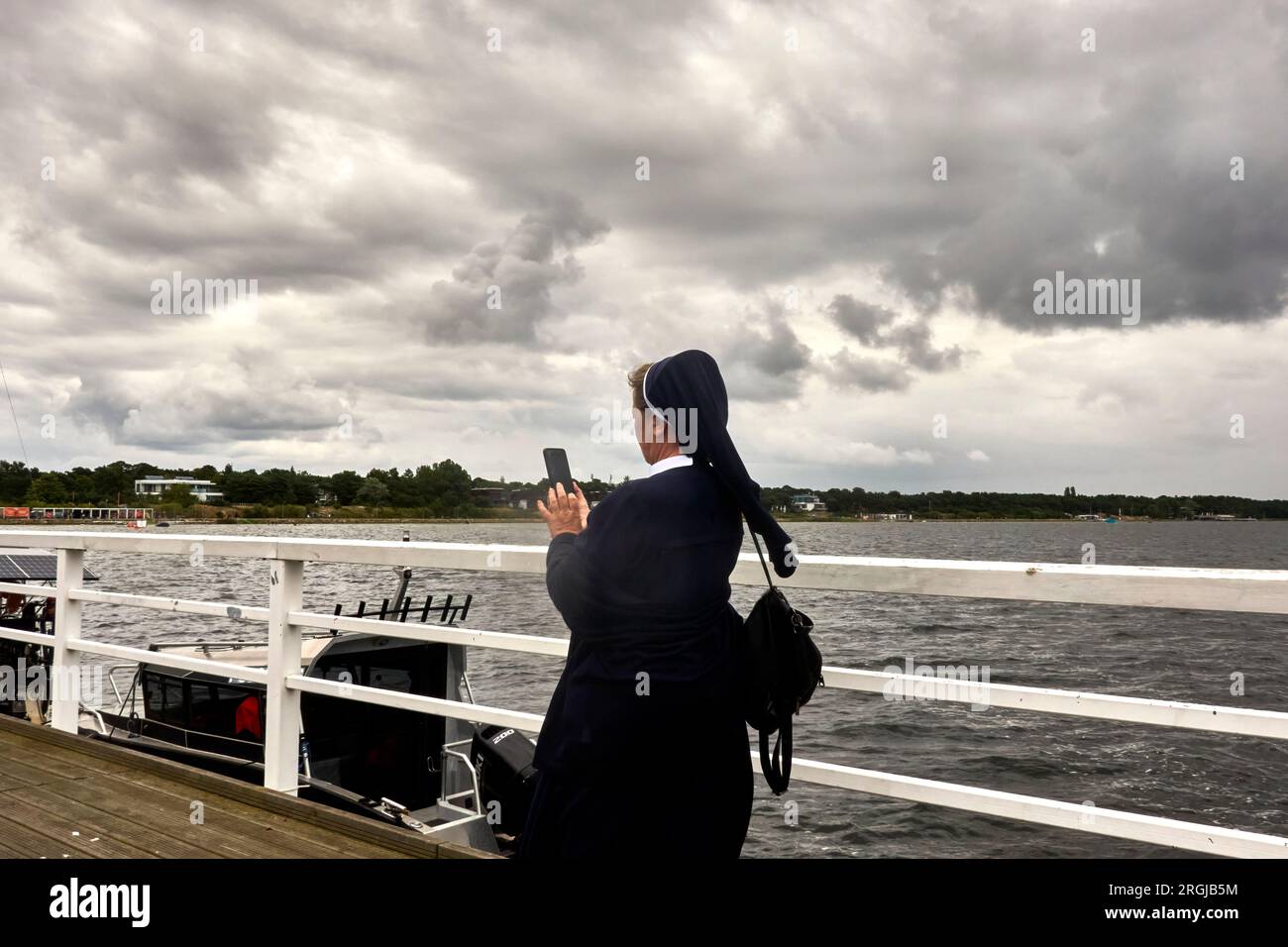 Hel, Polen, 19. Juli 2023: Nonne mit Handy auf einem Pier auf der Halbinsel Hel bei bewölktem Wetter Stockfoto