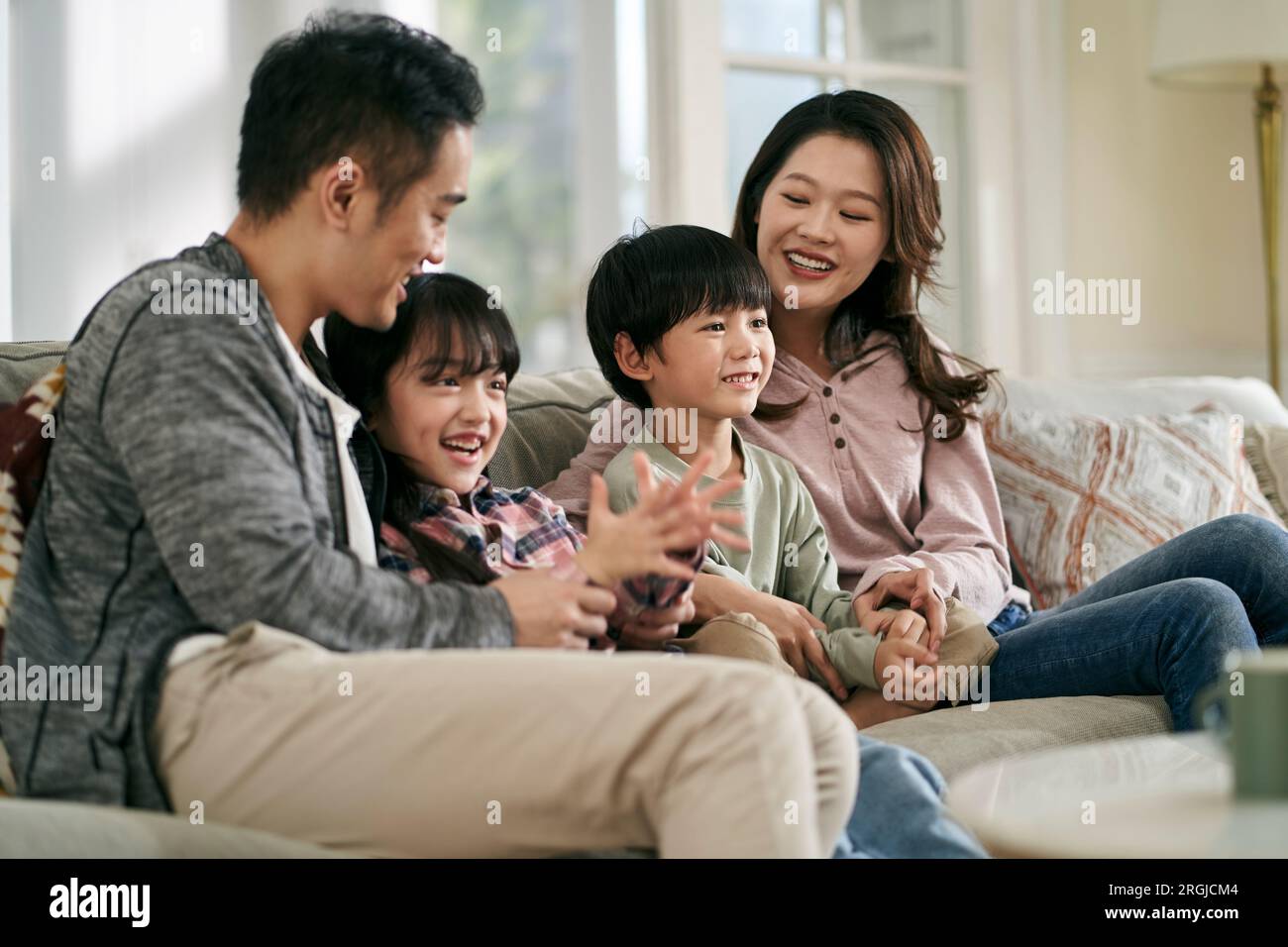 Glückliche asiatische Familie mit zwei Kindern, die zu Hause auf der Couch sitzen und zusammen fernsehen Stockfoto
