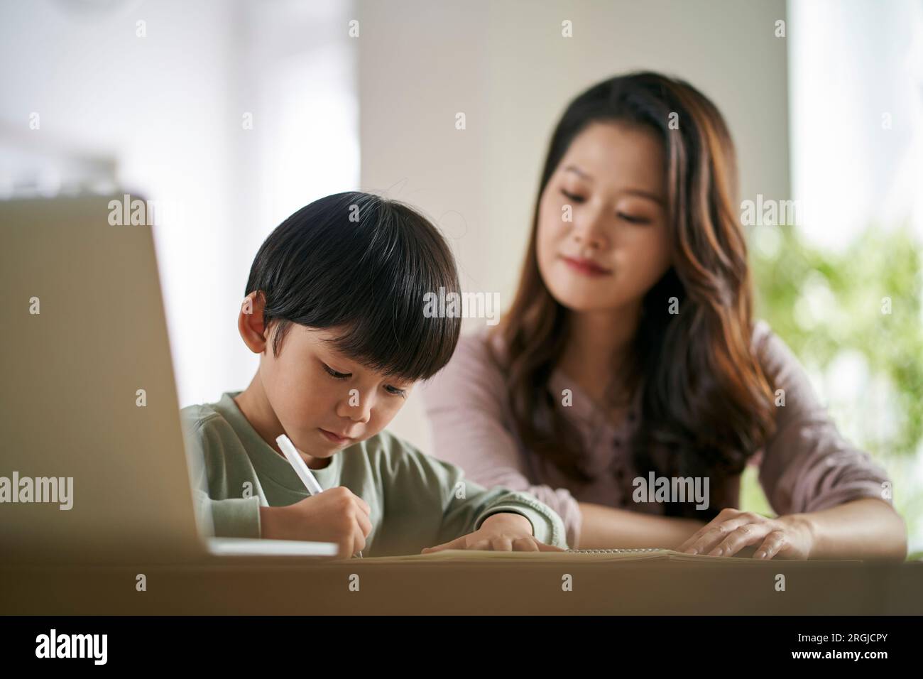 Junge asiatische Mutter, die zu Hause am Tisch sitzt und dem Sohn beim Lernen hilft Stockfoto
