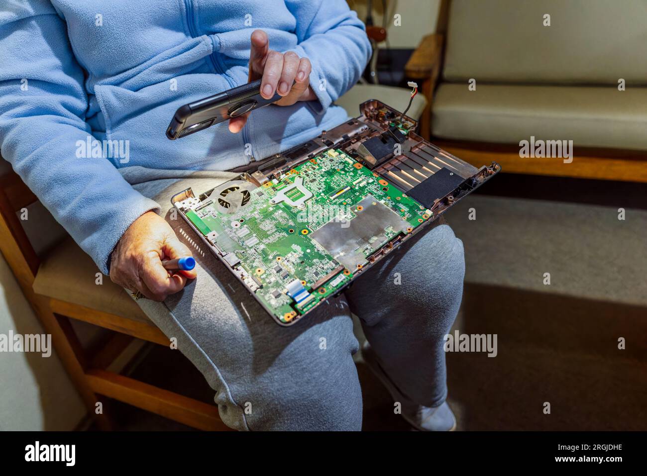 Computerreparaturen, alte Frau in den Siebzigern reparierte ihren Laptop, hielt die Telefonleuchte, um besser zu sehen Stockfoto
