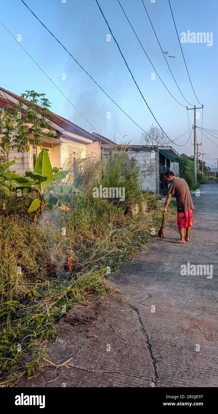 Bogor, Indonesien - 01. August 2023: Ein Mann räumte das Gras am Straßenrand und zündete es an Stockfoto