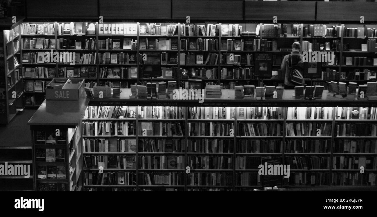 Breite, Schwarzweiß-Aufnahme von Bücherregalen, die von einem einzigen Käufer durchsucht werden. Stockfoto