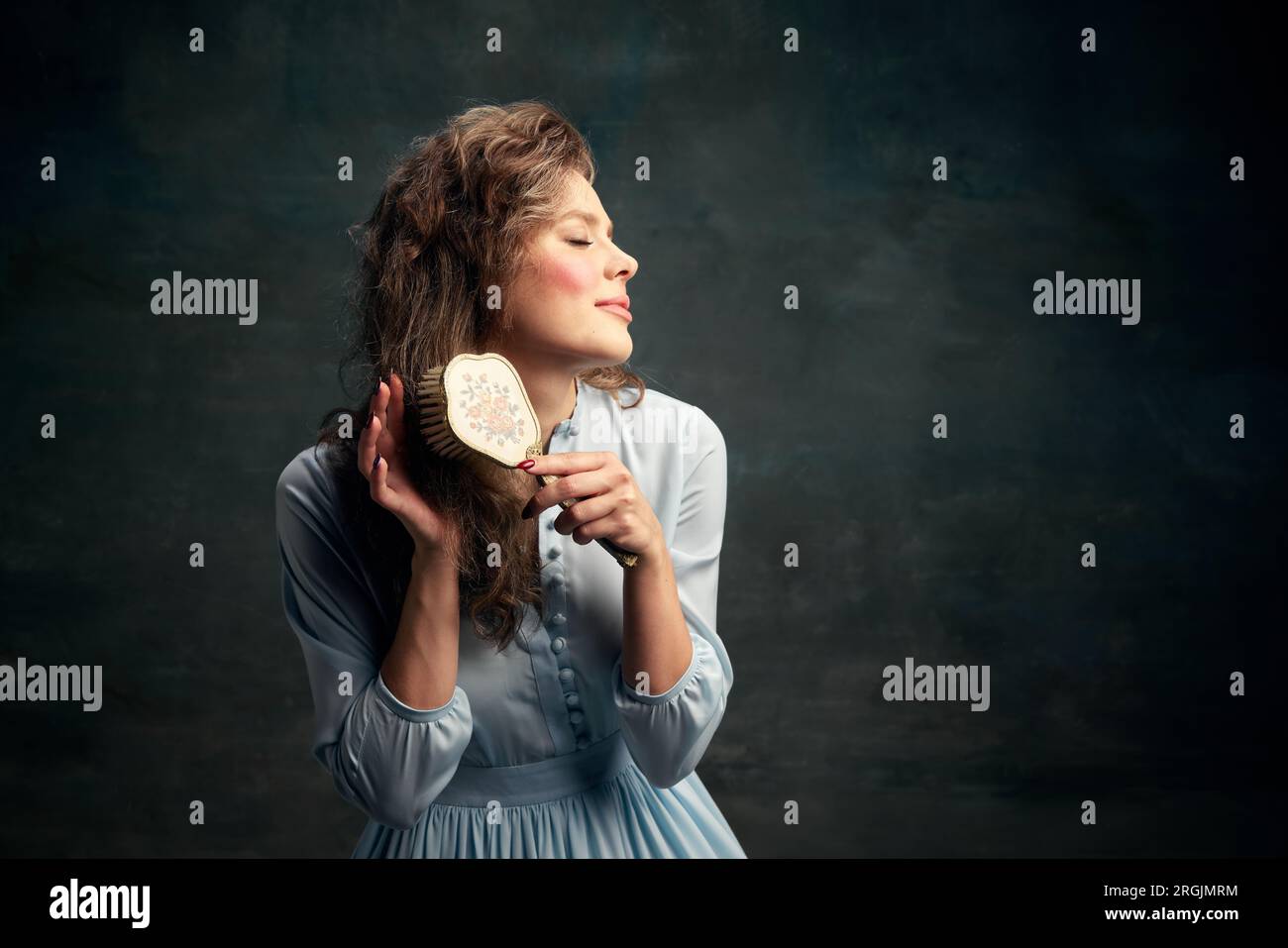 Porträt charmante aristokratische Frau in blauem historischen Kleid, hält eine alte Haarbürste in der Hand und bürstet ihr Haar. Stockfoto