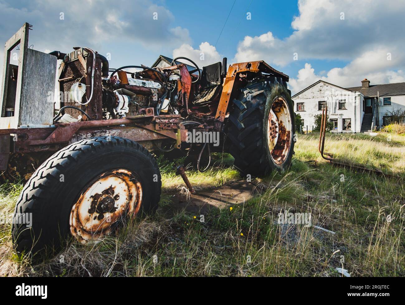 Alter Traktor mit fehlenden Karosserieteilen, da rostige Motor- und mechanische Teile sichtbar sind. Ein aufgegebenes landwirtschaftliches Fahrzeug vermittelt einen Rückgang des Anbaus Stockfoto