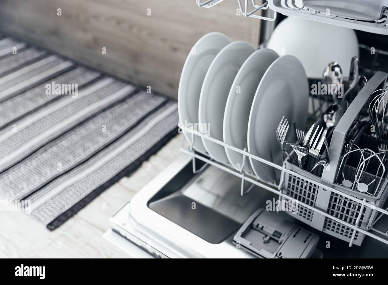 Vervollständigung der geöffneten automatischen Edelstahl eingebauten Geschirrspülmaschine in der modernen Küche mit sauberem Utensil. Weiße Teller, Geschirr, Becher, Metallgabeln und Messer. Haushalt, Haushalt, Hausarbeit Stockfoto