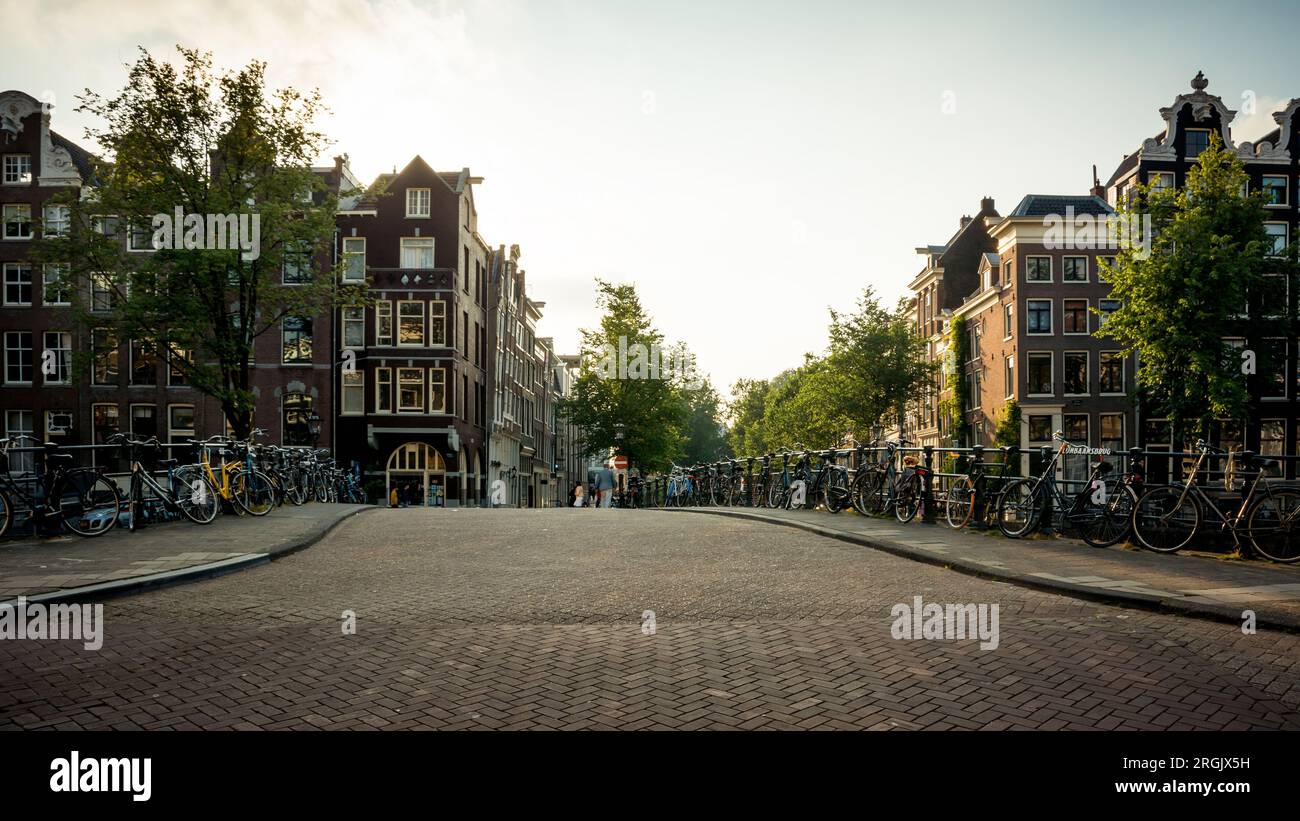 Brücke über den Kanal in Amsterdam am Samstagnachmittag. Zahlreiche Fahrräder parken in der Nähe des Geländers und einige Fußgänger laufen im Hintergrund Stockfoto