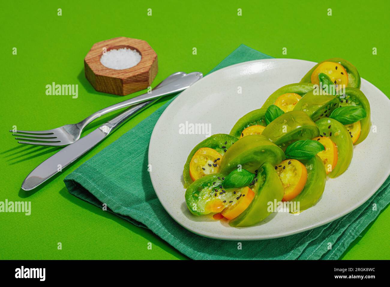 Frischer Sommersalat aus grüner Erbtomate Kiwi, frische Basilikumblätter und natives Olivenöl extra. Gesundes Lebensmittelkonzept, hartes Licht, dunkler Schatten. Brigg Stockfoto