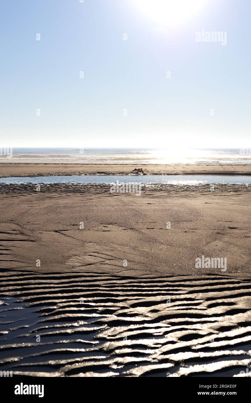 Wellen im Sand im Vordergrund und Ozean im Hintergrund, unter einem sonnigen Himmel. Stockfoto