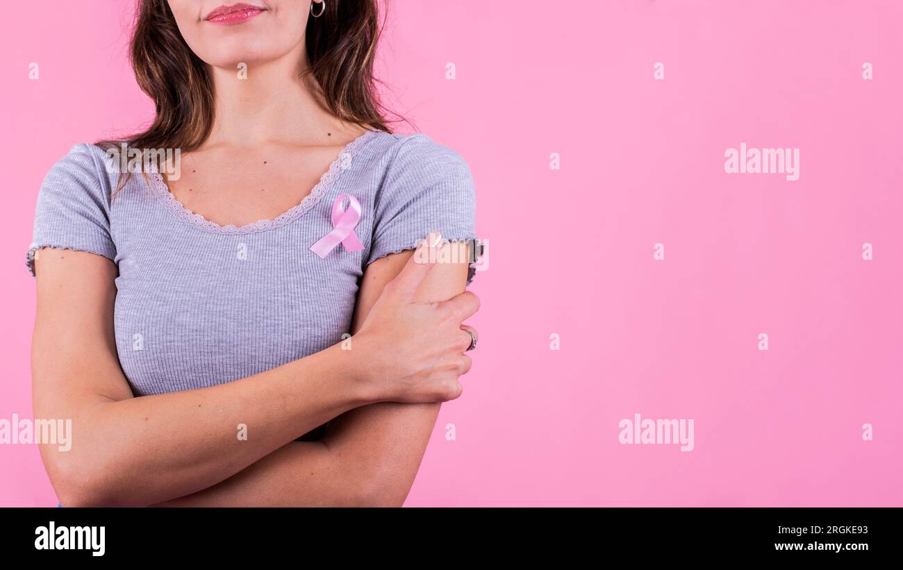 Ein pinkfarbenes Abzeichen-Band auf der Brust einer Frau, das Brustkrebs verursacht Stockfoto
