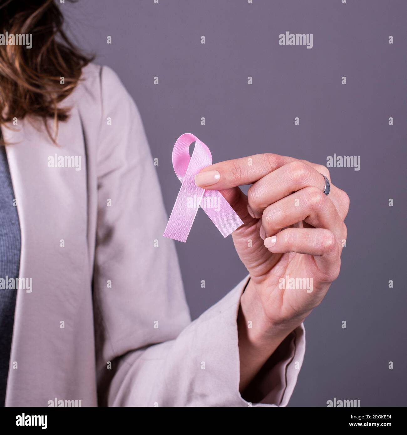 Ein rosa Abzeichen-Band, das eine Frau hält, um Brustkrebs zu unterstützen. Stockfoto