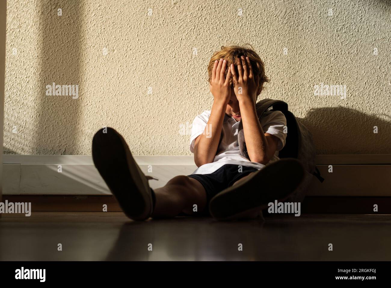 Besorgte Schüler, die allein auf dem Boden mit Rucksack im Klassenzimmer sitzen und das Gesicht bedecken, fühlen sich frustriert Stockfoto