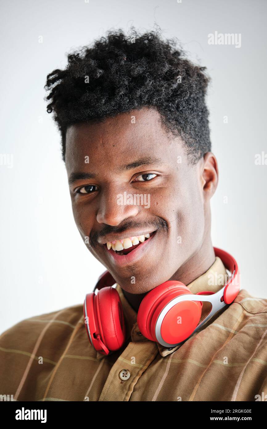 Lächelnder afroamerikanischer Mann mit afroamerikanischem Haarschnitt und modernem Headset im karierten Hemd und Blick auf die Kamera Stockfoto