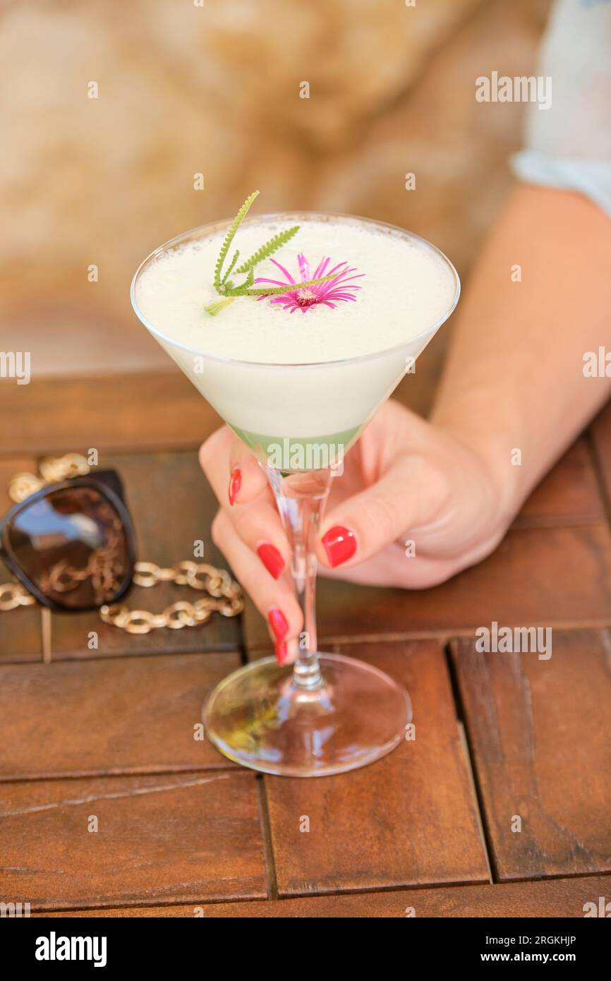 Aus einem hohen Winkel, eine Frau, die sich nicht wiedererkennt, nimmt ein Glas erfrischenden Cocktail mit Dekoration auf einem Holztisch Stockfoto