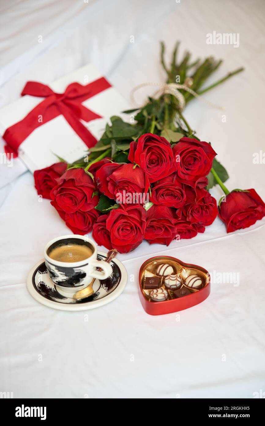 Von oben: Romantisches Geschenk bestehend aus einem Strauß roter Rosen, einer Tasse frischen Kaffees und einer herzförmigen Schachtel Pralinen im Bett Stockfoto