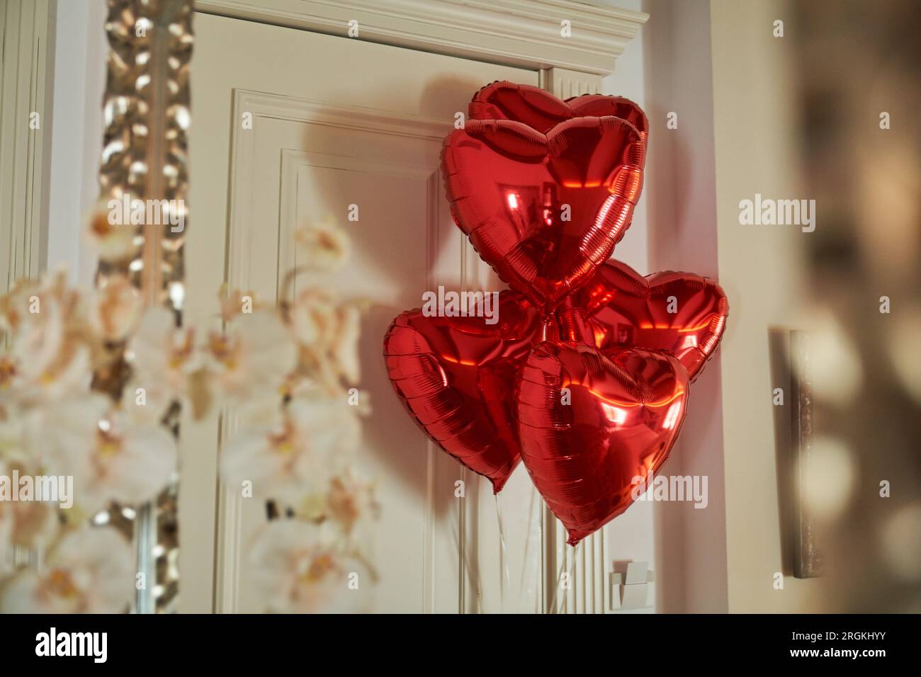 Glänzende rote herzförmige Ballons schmücken die Eingangstür der luxuriösen Hotelsuite im Urlaub Stockfoto