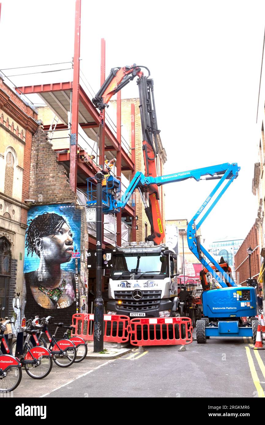 Straße gesperrt durch Baulastwagen mit Kran und Kirschpflückwagen Black WOMAN Wandgemälde Spitalfields East London E1 England KATHY DEWITT Stockfoto