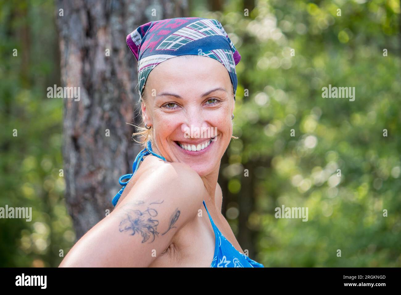 40 Jahre alte europäische Frau im Kopftuch und Badeanzug lächelt freundlich in die Kamera. Tourist im Wald im Urlaub Stockfoto