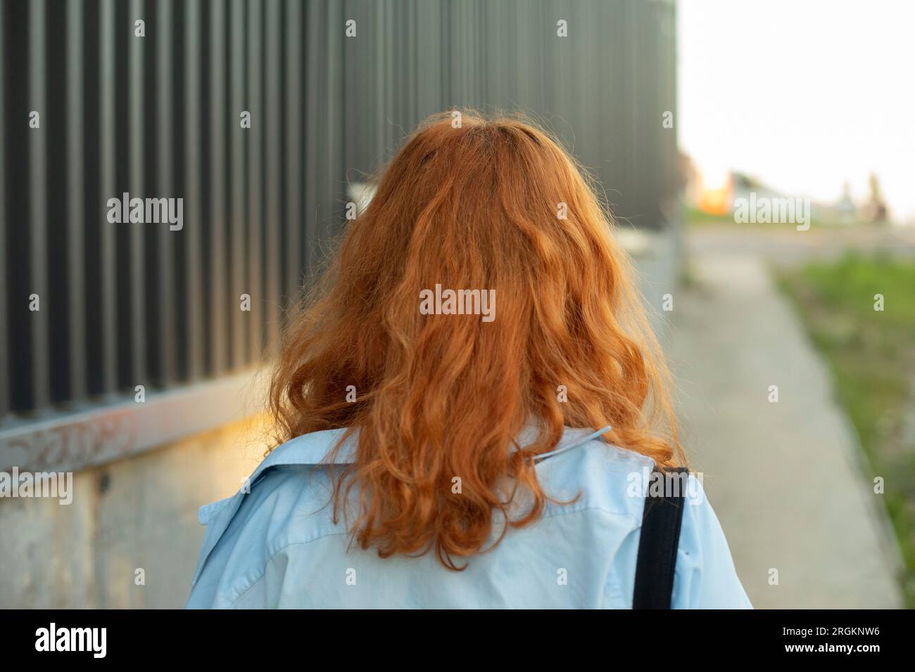 Ein Mädchen mit roten Haaren läuft im Sommer auf der Straße. Rote Haare. Der Student kehrt in der Stadt nach Hause zurück. Details des Spaziergangs. Stockfoto