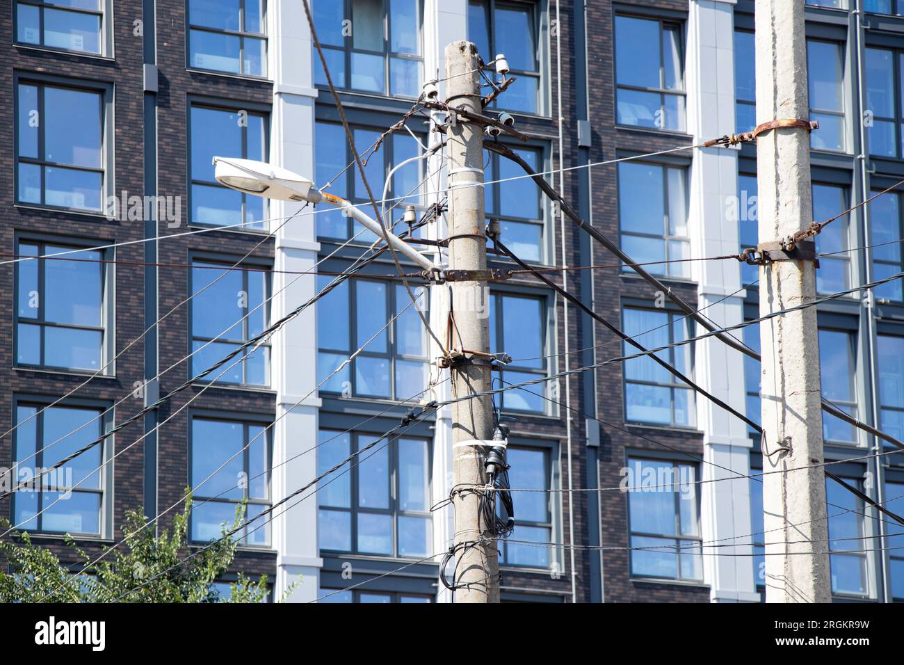 Stadtmast mit verschiedenen Kabeln und Drähten und Straßenbeleuchtung im Hintergrund der Fassade eines Wohngebäudes in der Ukraine im Sommer Stockfoto