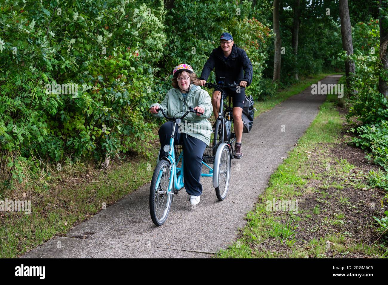 Meerhout, Antwerpen, Belgien - 1. August 2023 - 40. Junge Frau mit Down-Syndrom, die mit ihrem Bruder im Wald das Dreirad fährt Stockfoto