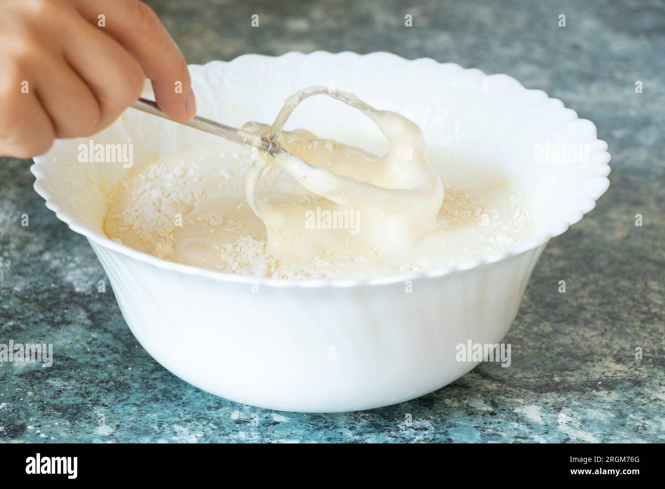 Wir schlugen die Eier mit Zucker auf einem Mixer auf einem Teller auf dem Tisch in der Küche und bereiten den Teig für den Kuchen vor Stockfoto