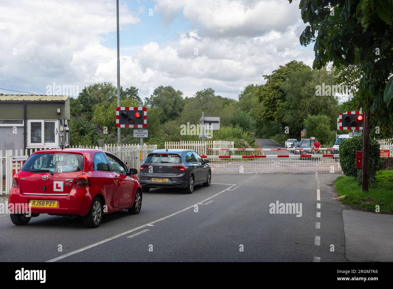 Der Bahnübergang in Kintbury, Berkshire, England, Großbritannien, mit Autos und einem Radfahrer, der darauf wartet, dass sich die Tore öffnen Stockfoto